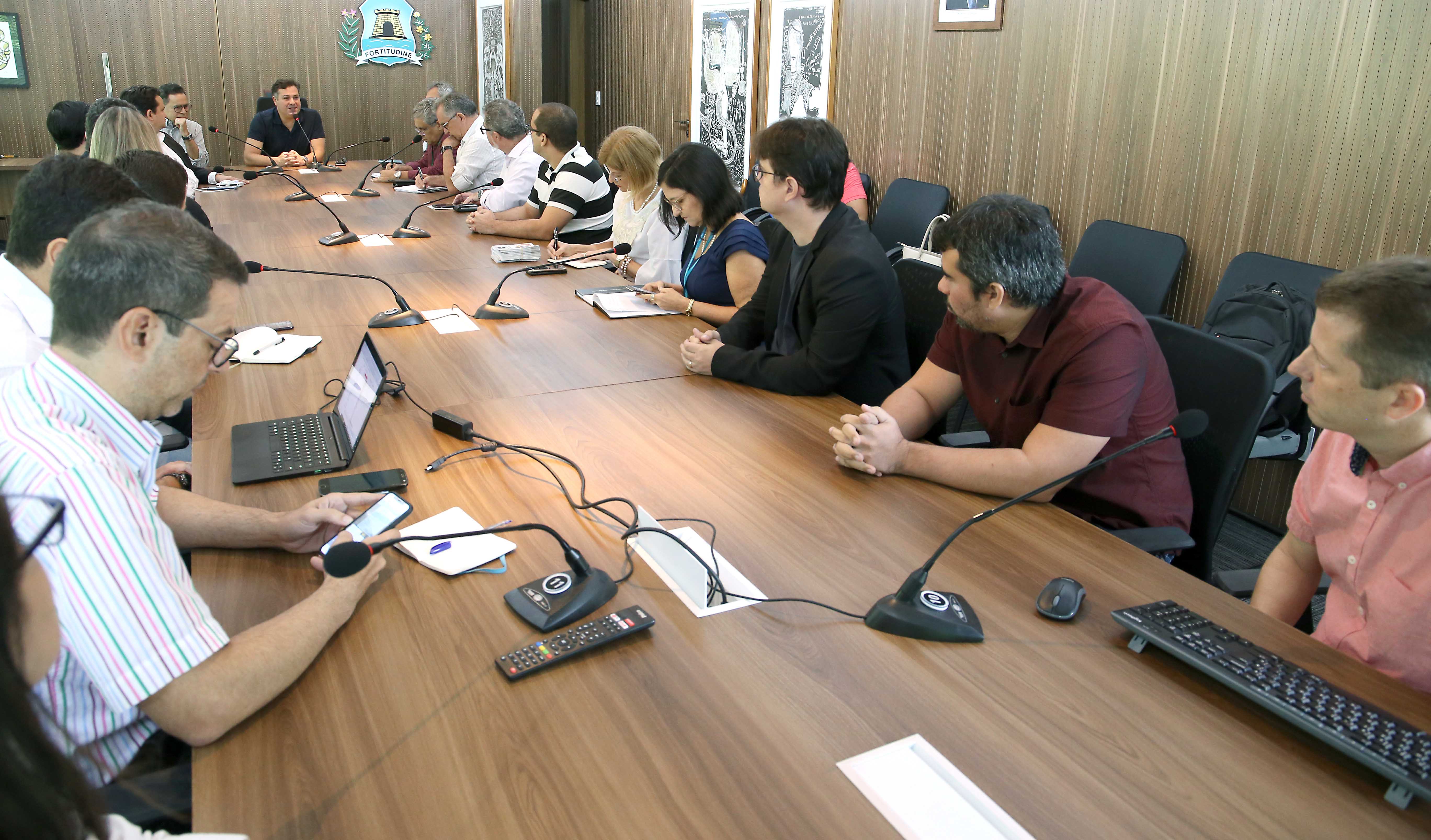 secretário samuel dias sentado em cabeceira de mesa com pessoas sentadas ao redor conversando